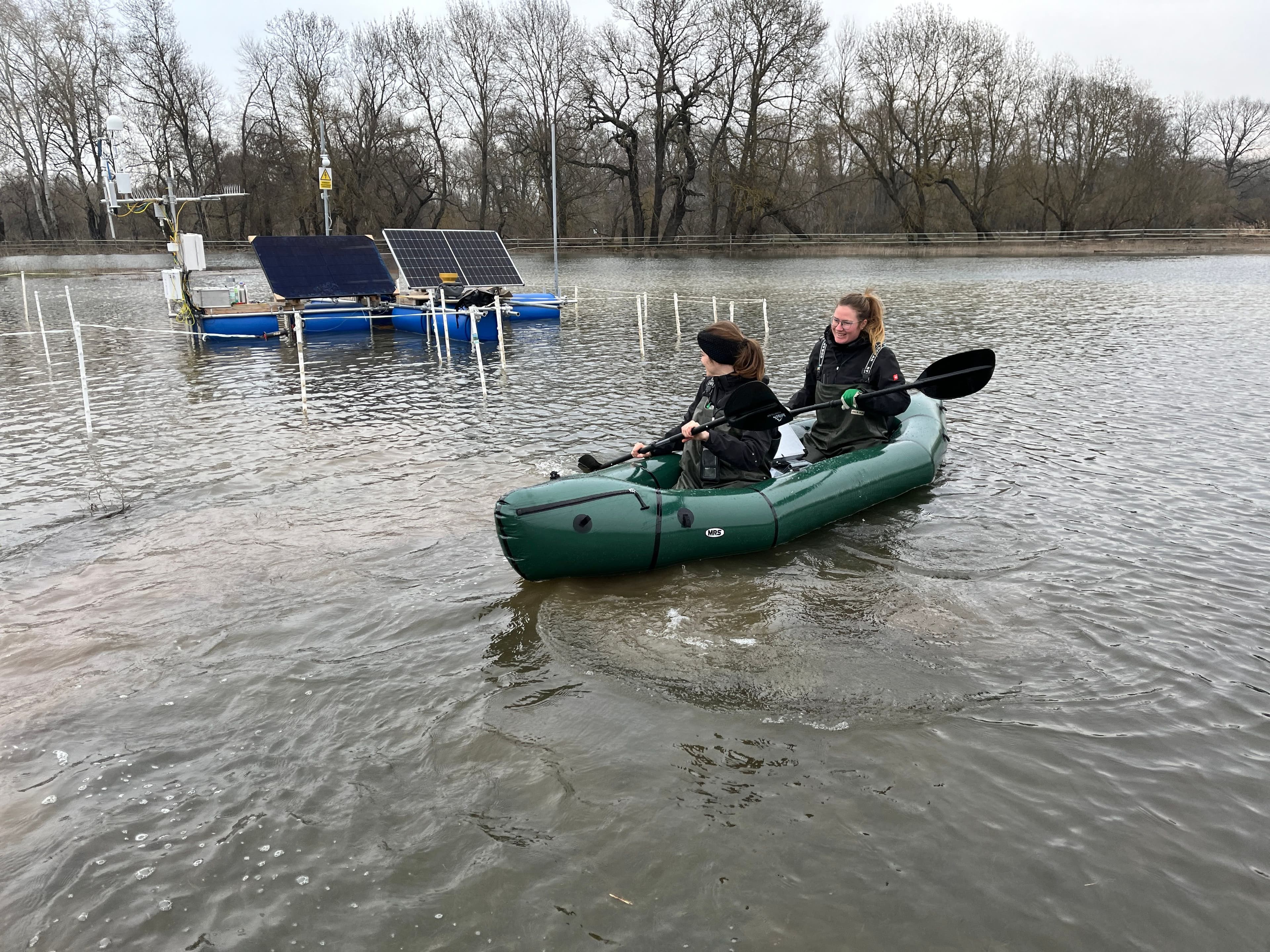 two women kayaking in the flooded field to check on the floating ec tower station