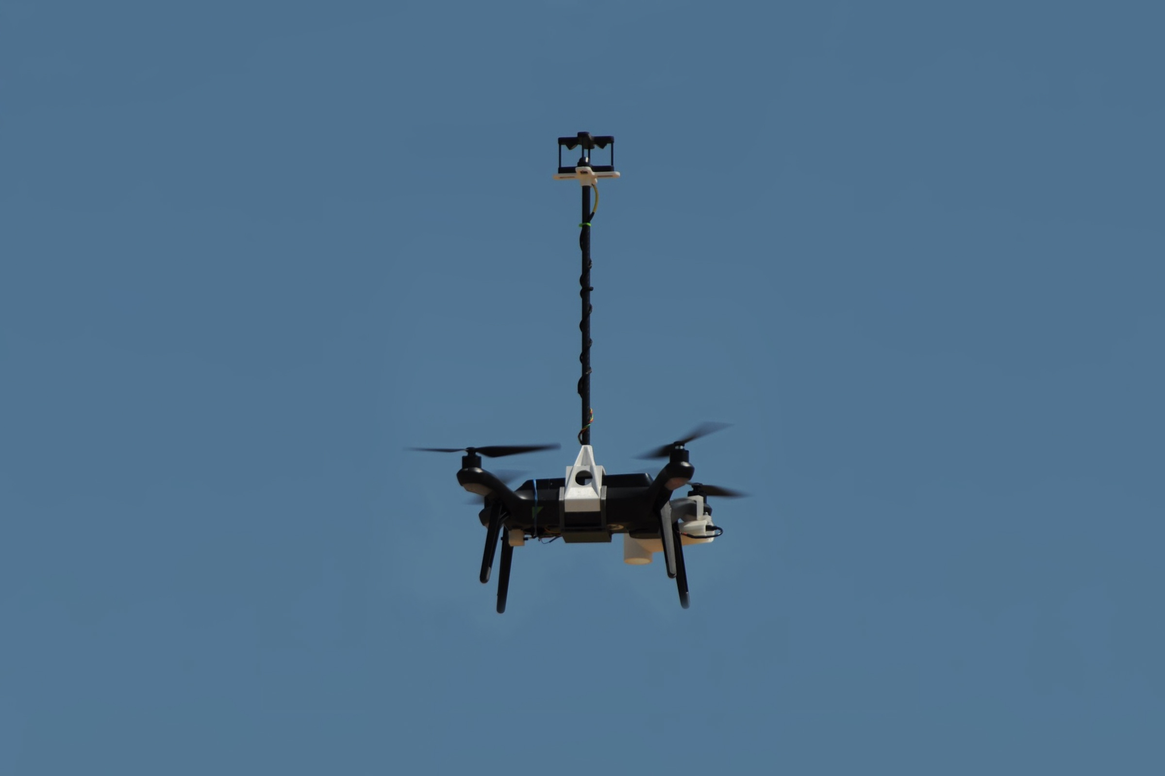 A drone (UAV) flies in the open air. A mast rises from the middle of the drone, supporting a TriSonica Mini Wind and Weather Sensor.