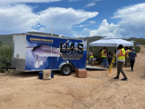 Embry-Riddle Aeronautical University UAS technology group carries the ground control station in trailer. The trailer is parked along a dirt road while the team prepares equipment under a sun shelter nearby.